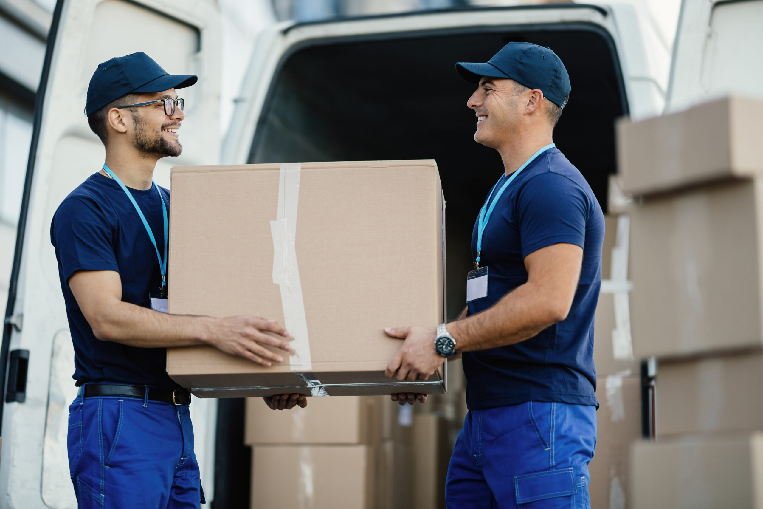 Happy manual worker cooperating while carrying cardboard boxes in a delivery van.